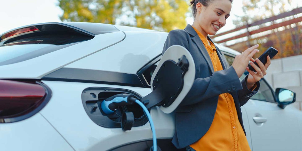 woman using mobile while car electric charging