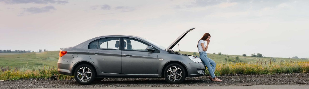  Woman sitting on a broken down car while on the phone.