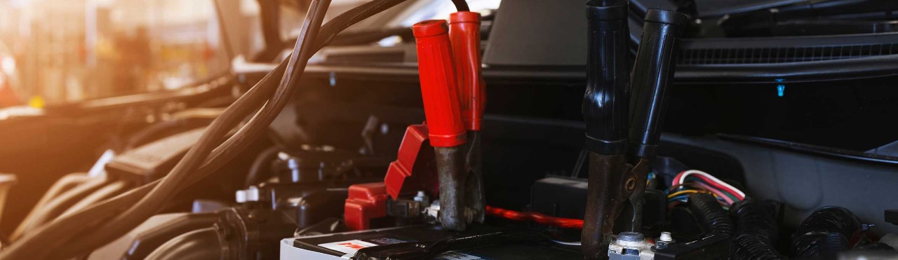closeup charging car battery with electricity through jumper cables with soft-focus and over light in the background
