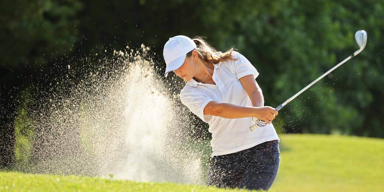 woman hitting golf ball in sand trap 