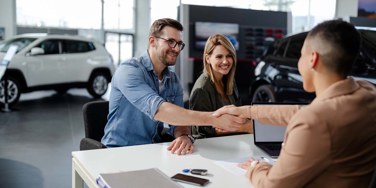  smiling couple buying a car at showroom 