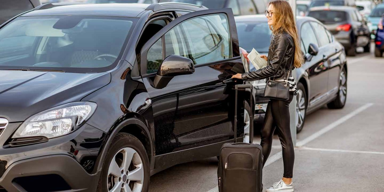 Young and happy woman walking with suitcase holding rental contract on the car parking
