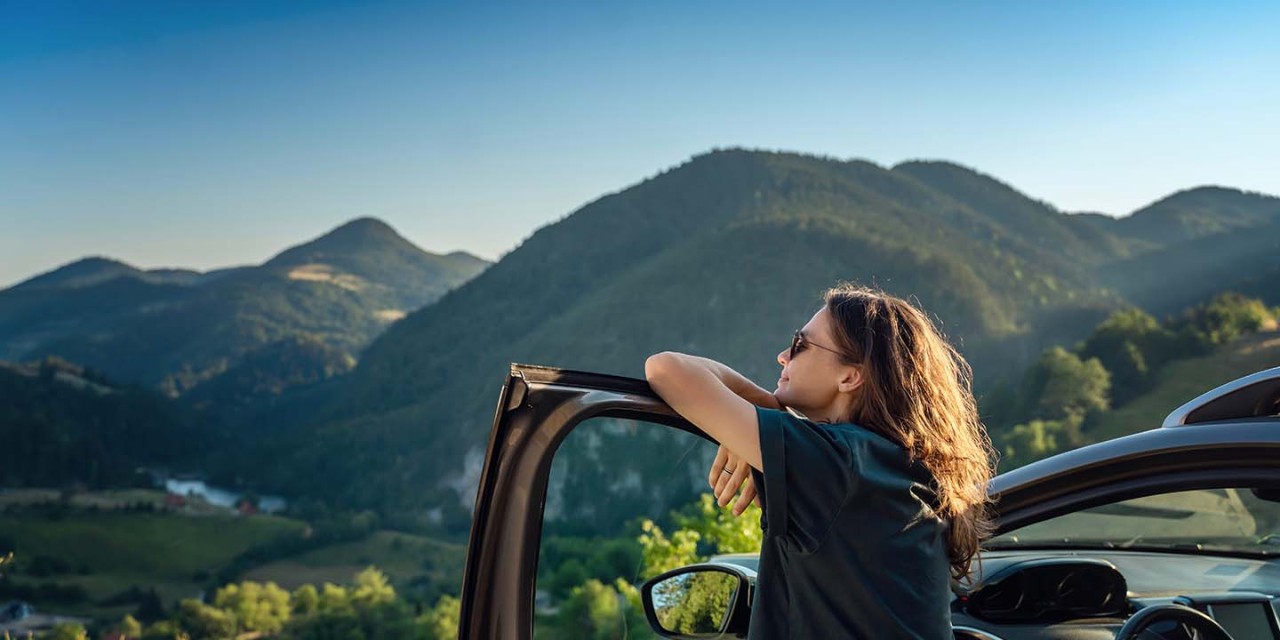 Young woman traveler near car watching a beautiful mountain view 