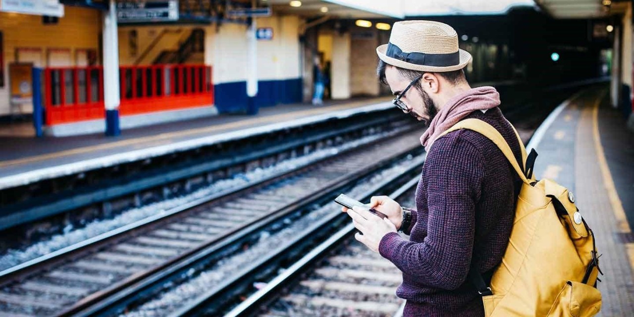  man looking at the mobile phone while waiting for the train