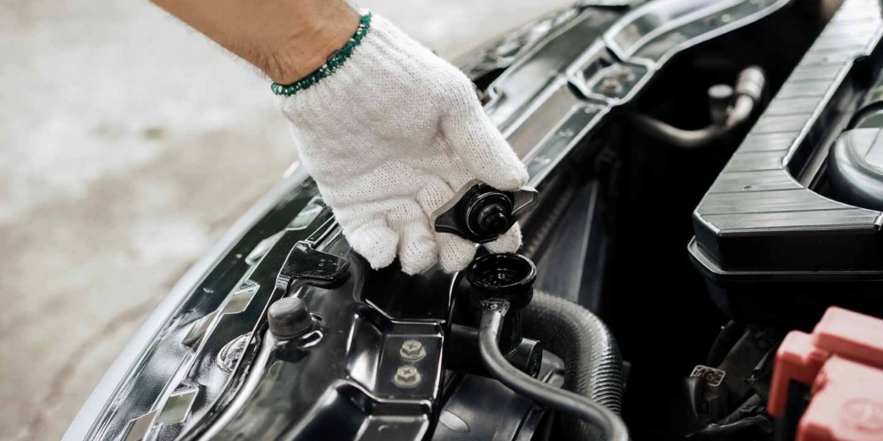 Close-up of hand of a gloved mechanic opening the radiator cap to check the coolant level