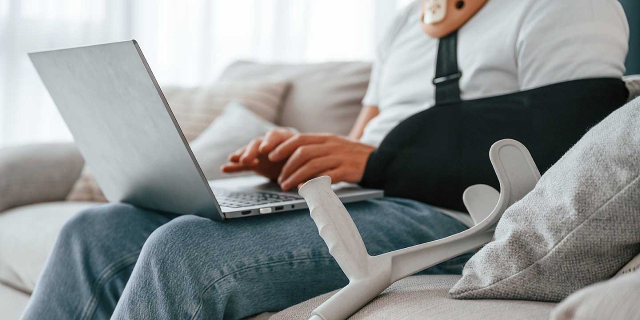 Sitting on the sofa with laptop. Man with crutches is at home indoors