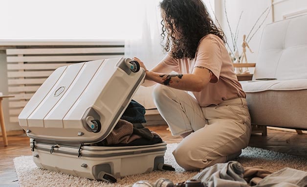 Young woman packing suitcase in the living room, preparing for travel