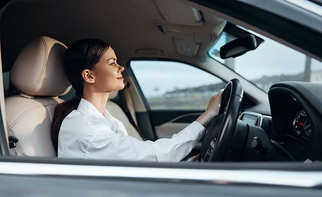 A woman is seated in the driver's seat of a car, hand on the steering wheel and focus while driving