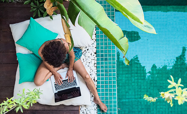 Top view of man working on laptop near pool in a vacation resort in tropical country. 