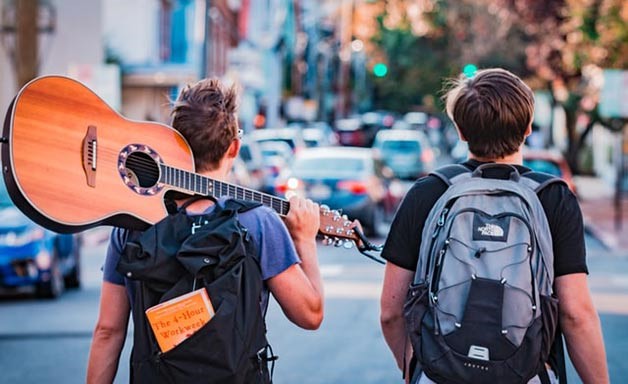 young men waking on the street with a guitar 