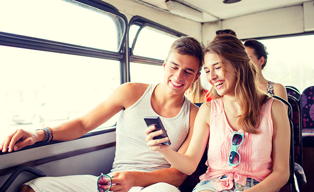 Happy couple having fun while using smart phone in a bus