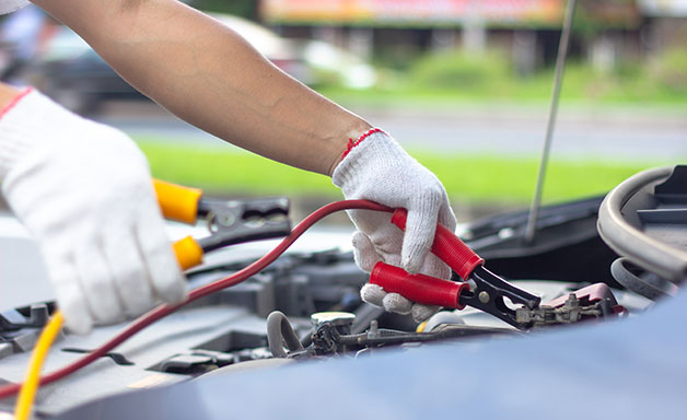 Car mechanic man using battery jumper cables to charge a dead battery.
